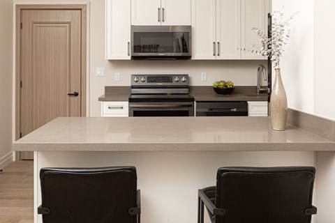 a kitchen with white cabinets and a counter with two black chairs